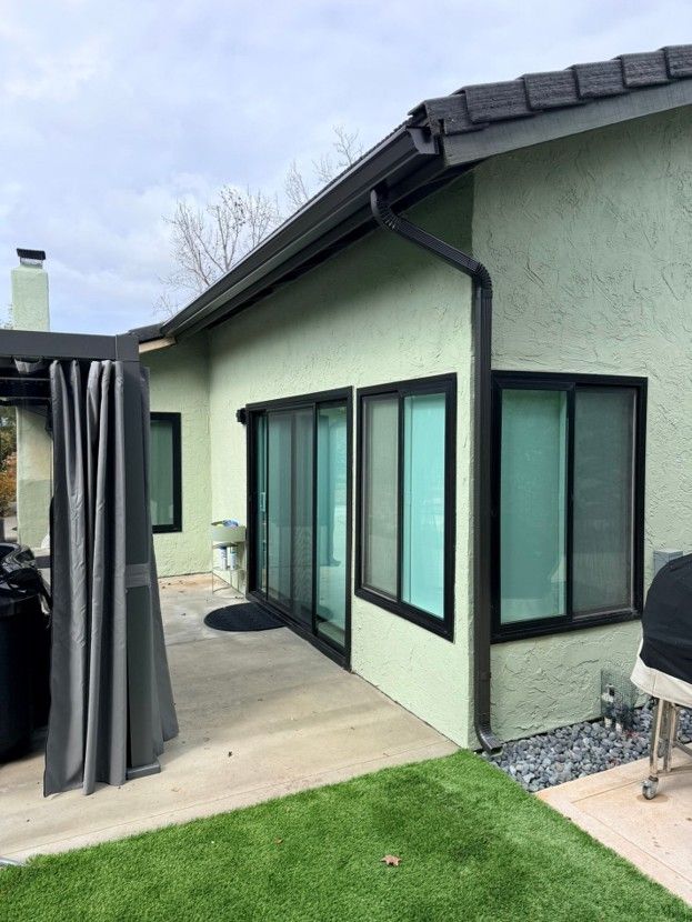 Modern house patio with sliding glass doors, gray curtains, and a small lawn under a cloudy sky