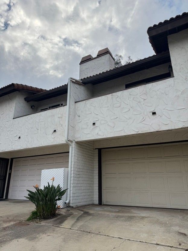 White stucco townhouse garages under a cloudy sky, with a small plant in the driveway