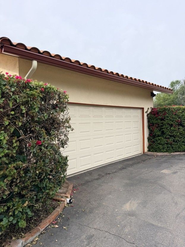 Garage door beside hedges and driveway under a tiled roof in a residential area