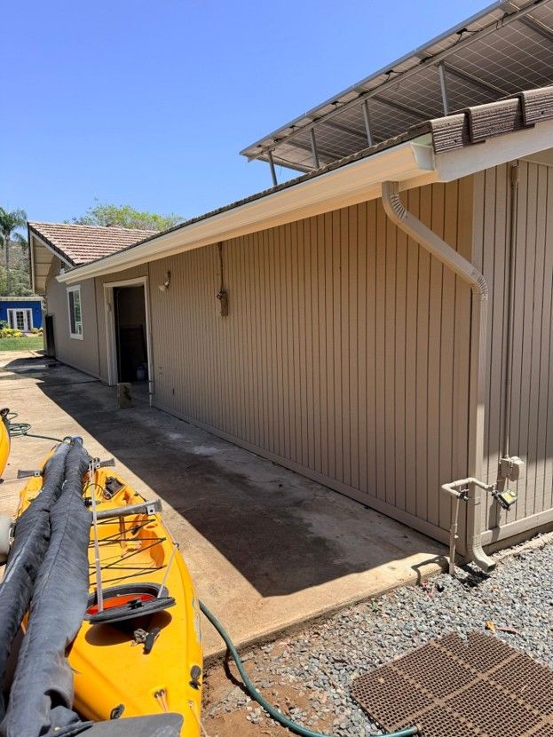 Tan building wall beside a paved walkway, with yellow equipment in the foreground and a roof overhang above.