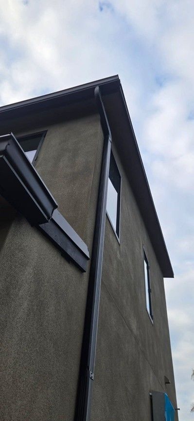Low-angle view of a gray house exterior with dark roof trim against a cloudy sky