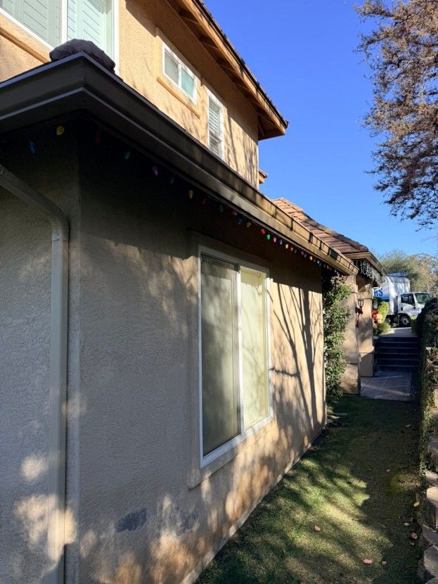 Side of a stucco house with windows, a stairway, and a grassy path under blue sky