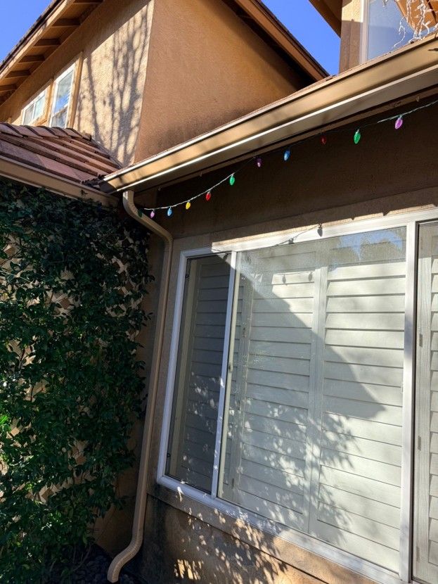 House exterior with white window shutters, tan siding, and colorful string lights under the eaves
