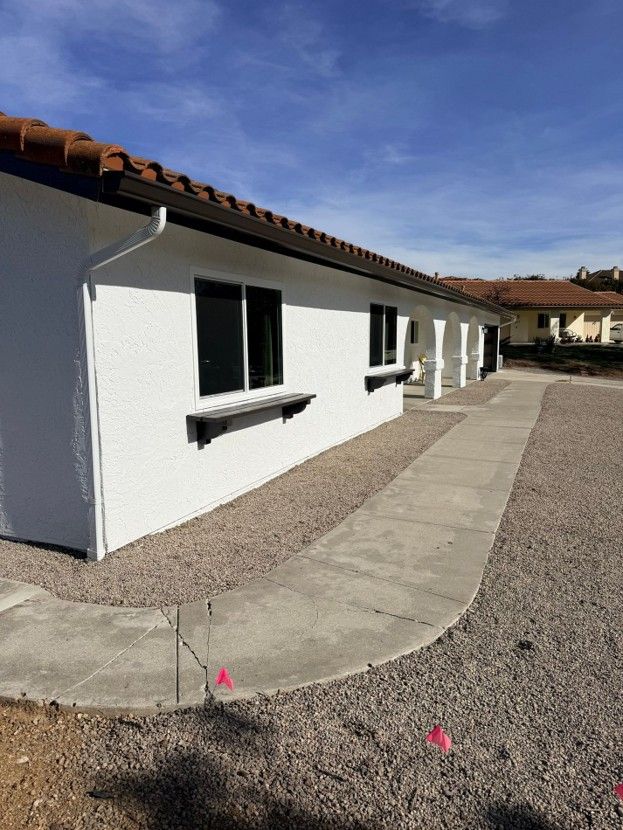 White single-story house with red tile roof and curved concrete walkway beside gravel yard