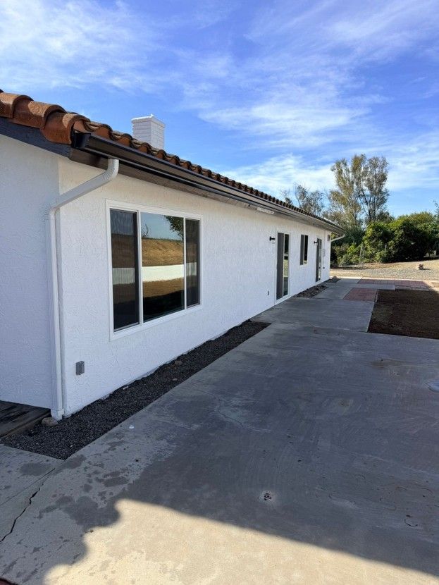 White stucco house exterior with brown tile roof and concrete driveway under a blue sky