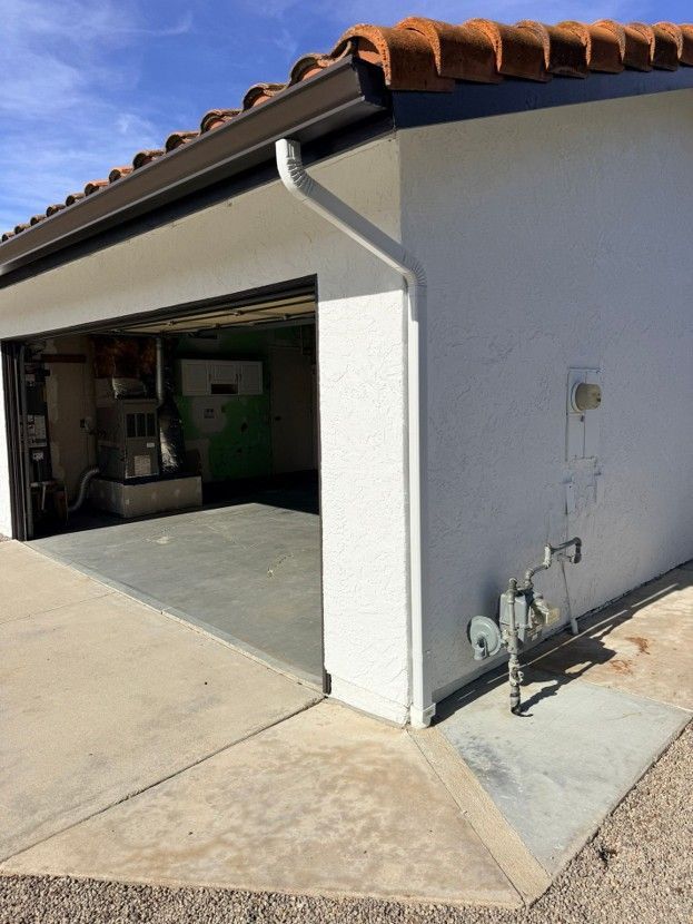 Exterior corner of a house with an open garage, white stucco walls, and visible gas meters on the side.