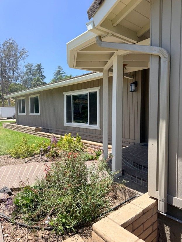 House exterior with white trim, tan siding, front windows, porch, and a small landscaped garden.