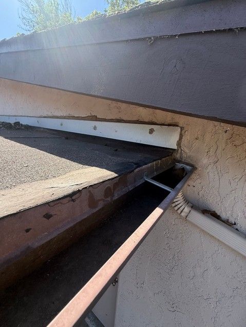Close-up of a damaged roof edge with exposed insulation, beams, and a gap under dark shingles