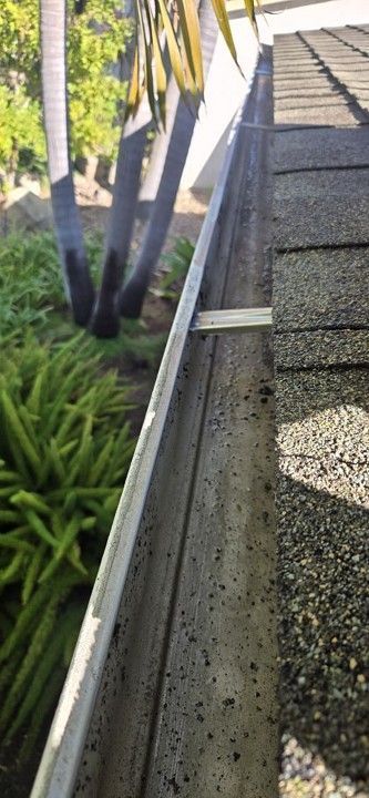 Metal railing beside a gravel path with plants and a concrete wall in sunlight