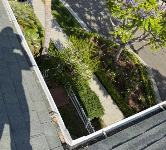 View from a rooftop onto a narrow landscaped courtyard with trees, shrubs, and sidewalks in sunlight