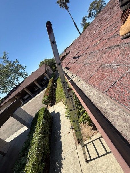 Tilted view of a red-roofed house, chimney, and hedge-lined yard under a clear blue sky