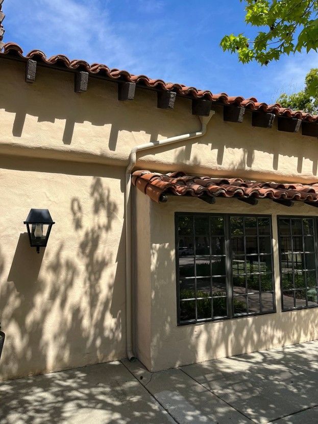 Stucco building exterior with terracotta roof tiles, black lantern, and large window in sunlight