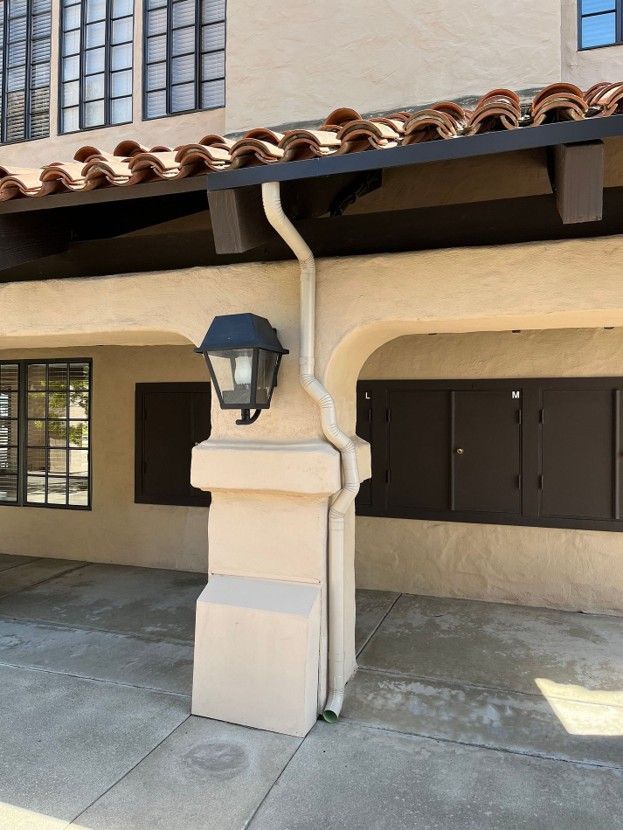 Spanish-style building entrance with beige stucco pillar, dark lantern, windows, and red tile roof eaves
