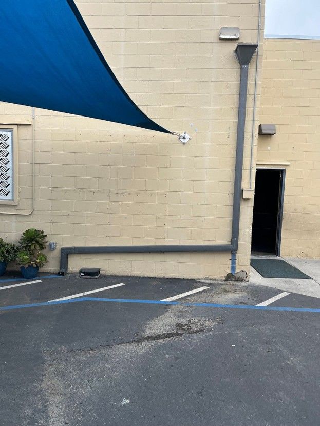 Empty parking lot beside a beige building with a blue shade canopy and an open doorway