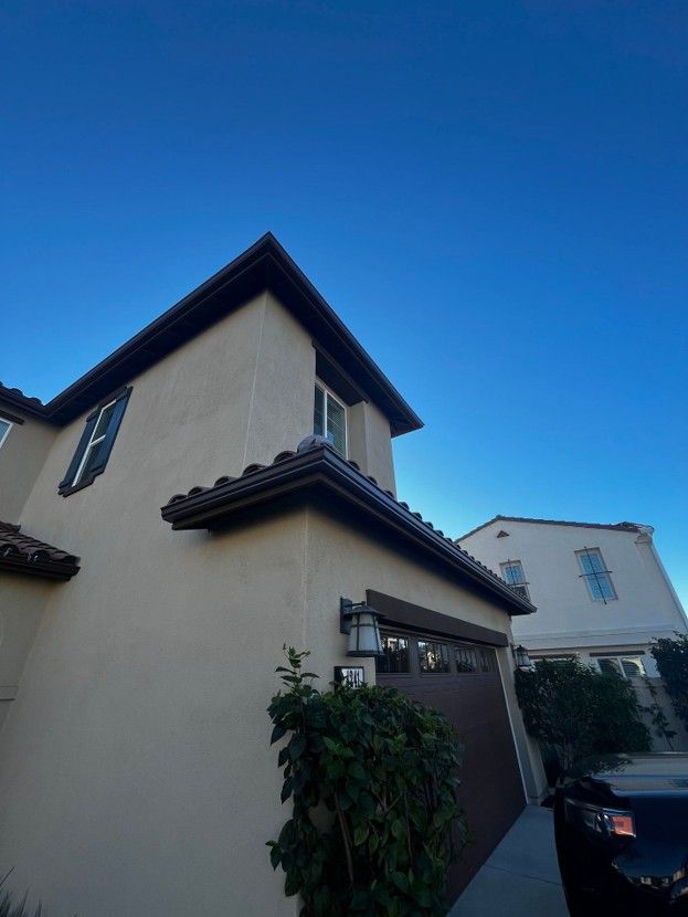 Two-story beige house with dark roof under a clear blue sky, viewed from a driveway with a car nearby