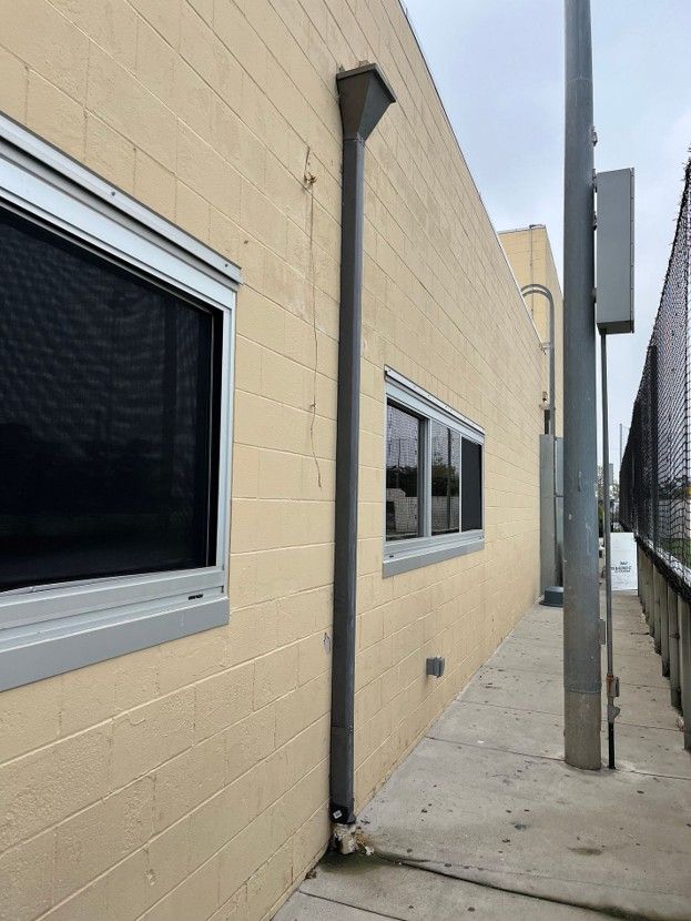 Narrow concrete walkway beside a beige building with windows, a utility pole, and a fenced area.