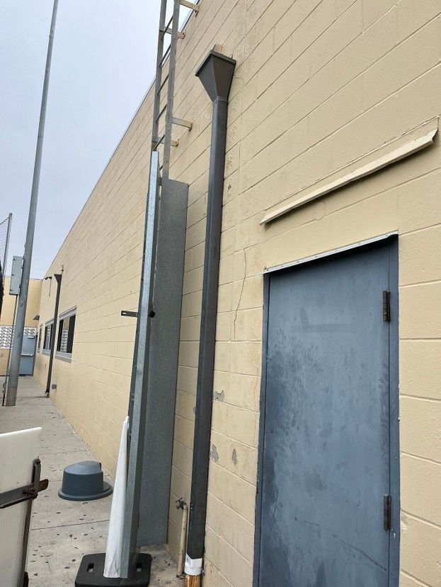 Gray utility box and conduit pipes beside a beige industrial building with a blue door.
