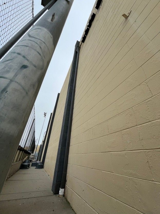 Narrow alley with a tall beige wall and a large utility pole on the left, viewed upward toward the sky
