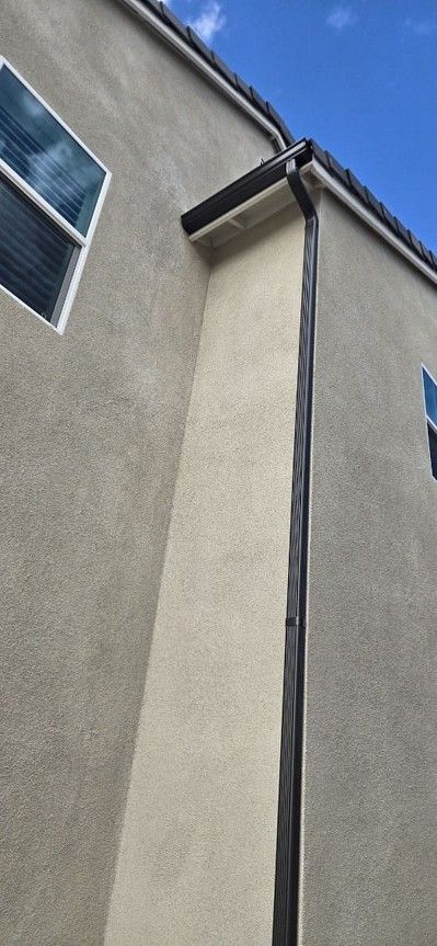 Close-up of a beige stucco building corner with a gray gutter and blue sky above