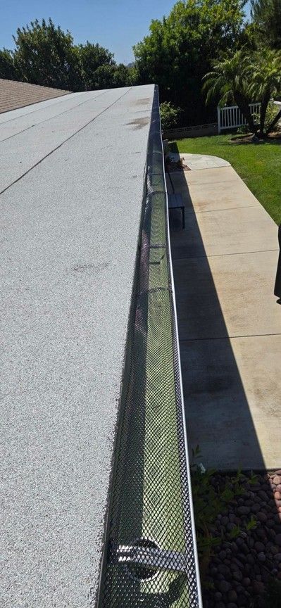 Rooftop gutter with green mesh leaf guard beside a sidewalk and lawn.