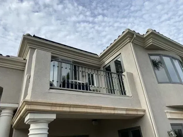 Exterior of a beige two-story house with a balcony and ornate trim against a cloudy sky
