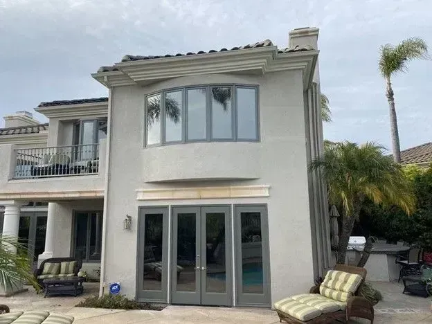 Two-story stucco house with glass doors, balcony, and palm trees in front yard