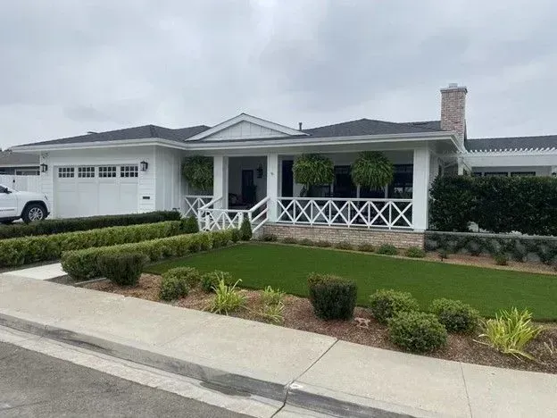 Suburban house with white porch, manicured lawn, and a garage on a quiet street