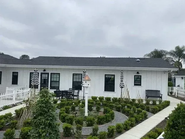 White cottage with landscaped garden, winding path, and outdoor seating under a cloudy sky