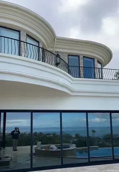 Modern white curved villa with glass balcony and windows overlooking a pool and landscape