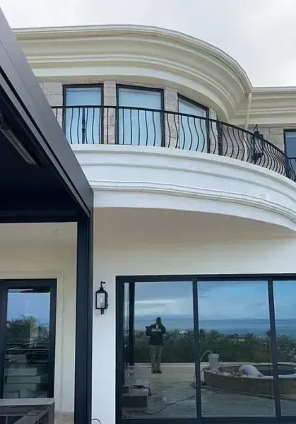 Modern two-story white house with curved balcony, black railings, and large glass doors beside a pool