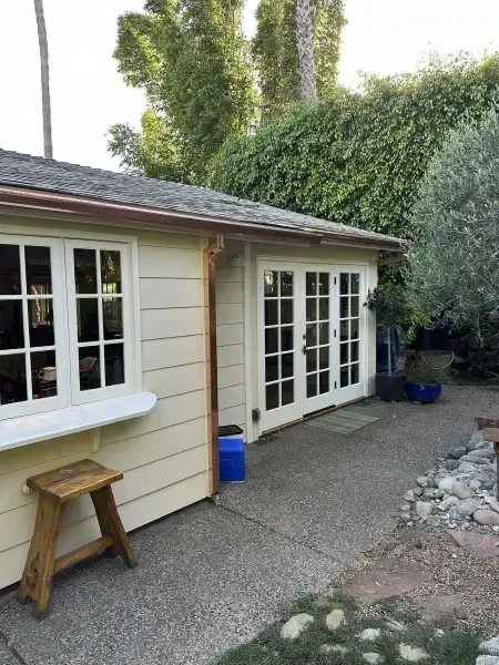 Backyard patio beside beige house with French doors, window, and a small wooden stool