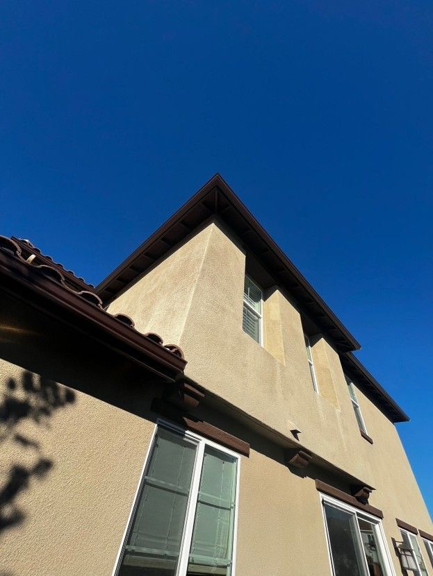 Low-angle view of a beige stucco house with a red-tiled roof against a clear blue sky