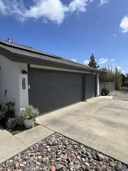 Modern home exterior with a gray garage door, driveway, and rock landscaping under a blue sky