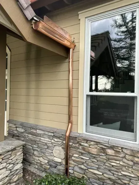 House exterior with beige siding, stacked-stone facade, and a copper downspout beside a window