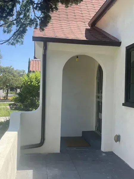 Arched house entryway with white walls, gray tiled porch, and red roof under a bright sky