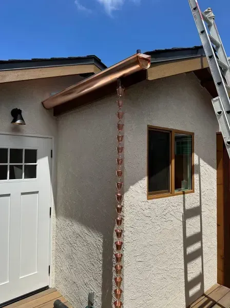 Exterior corner of a house with stucco walls, white garage door, wooden window, and copper roof trim under construction