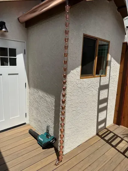 House corner with white stucco, white door, window, wood deck, and a green leaf blower on the ground