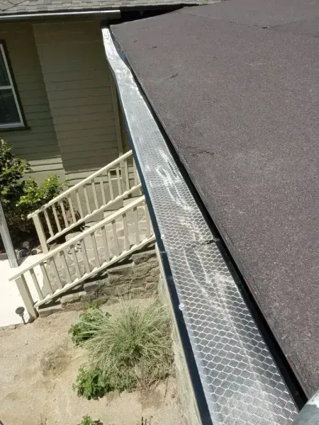 Gutter and roof edge beside a beige house, with a white railing and steps below.