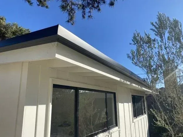 White house exterior with dark roof trim, large windows, and trees against a blue sky