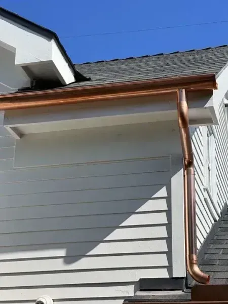 House exterior with white siding, gray roof, and copper downspout against a blue sky
