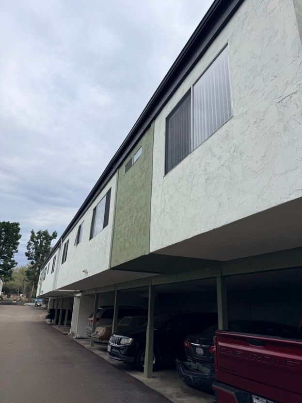 Apartment building with covered parking spaces and parked cars along a paved driveway
