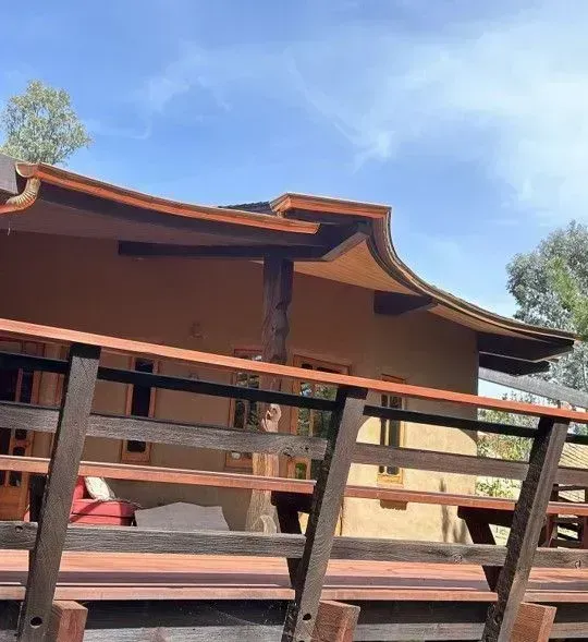 Traditional wooden building with curved roof and open porch behind a wooden fence under a blue sky