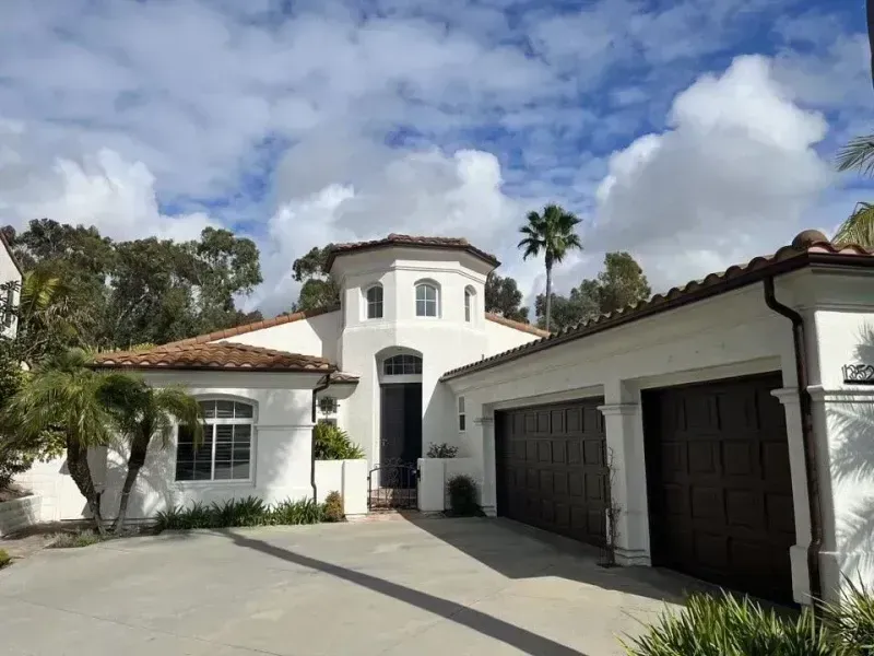 White stucco house with a tiled roof, two-car garage, and a clear blue sky above the driveway