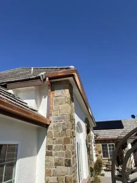 Stone house exterior with white walls, brown roof trim, and clear blue sky.