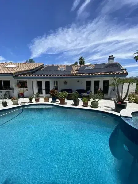 Luxury backyard with curved blue pool, white patio, potted plants, and a tiled house under a bright sky
