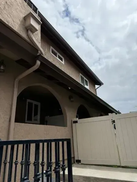 Residential house with arched porch, white gate, and dark blue fence under a cloudy sky
