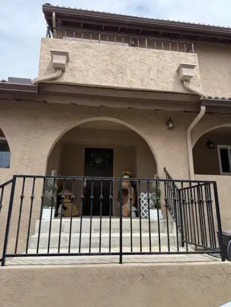 Front entrance of a beige building with an arched porch and black metal railing