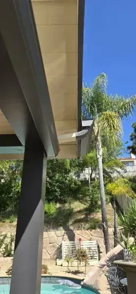 Modern house exterior with a covered patio, palm tree, and hillside landscaping under a blue sky