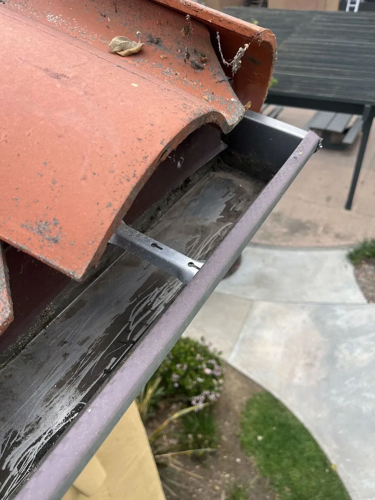 Close-up of a rusted metal gutter with debris and a loose roof edge