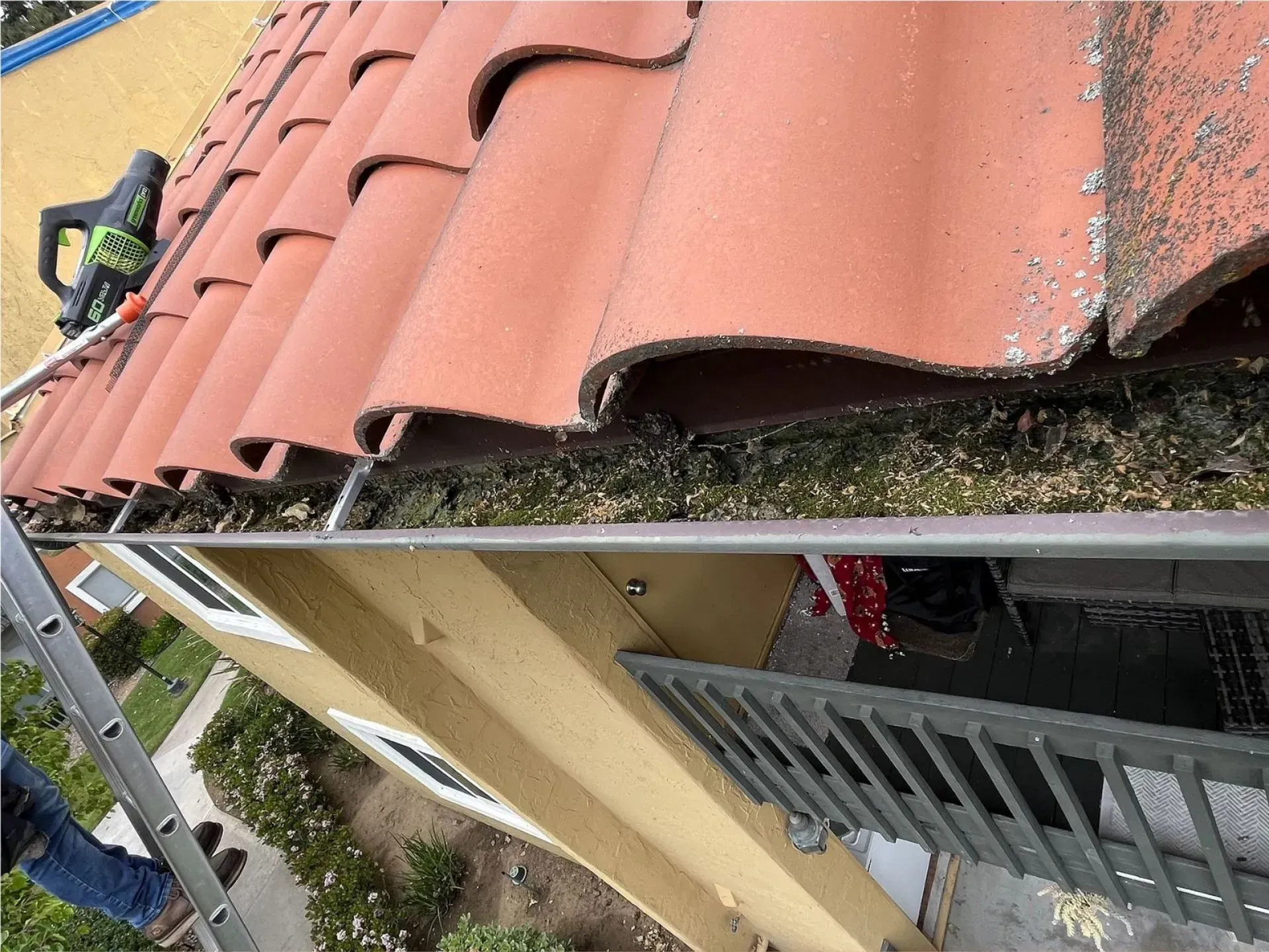 Damaged red roof tiles and exposed eaves on a house exterior, with a worker below.